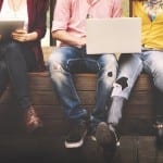 Diverse group seated with tablets and laptops, casual attire, focus on legs and devices.