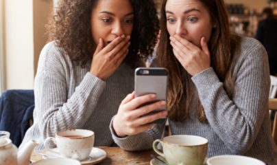 two women looking at a phone with their hands over their mouth